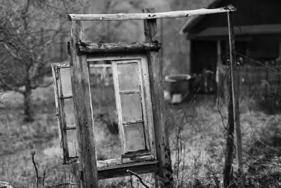 Schwarz-Weiß Aufnahme; zeigt einen alten, verwitterten Fesnterrahmen, der als "Dekorationsobjekt" auf einem Gartengrundstück steht.