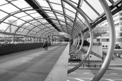 Schwarz-Weiß Aufnahme; zeigt die tunnelartige, aus zahlreichen Quer- und Längsstreben bestehende Stahlkonstruktion, die vor dem Haupteingang der Universität Bielefeld als Fußgänger-Überweg gebaut wurde.