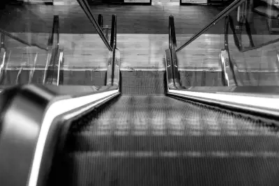 Schwarz-Weiß Aufnahme; zeigt eine Rolltreppe mit leuchtenden Rändern und in einer Perspektive von oben nach unten.