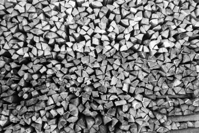 Schwarz-Weiß Aufnahme. Zeigt einen relativ großen, aufgeschichteten Holzstapel.
