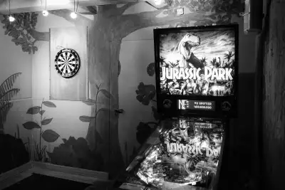 Schwarz-Weiß Aufnahme. Zeigt eine Dartscheibe und einen Flipper-Automaten im Nebenraum einer kleinen Kneipe.