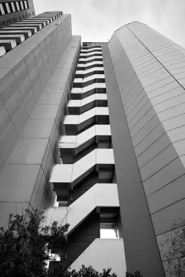 Schwarz-Weiß Aufnahme; zeigt die neben einem Hochhaus angebrachte Notausstiegstreppen, die zugleich mit einem Wasserspeicher(turm) verbunden sind.