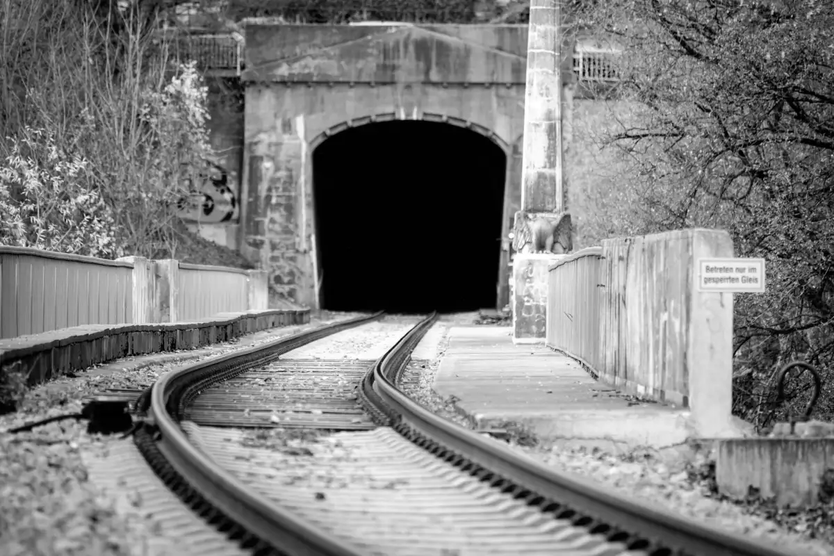 Schwarz-Weiß Aufnahme; zeigt die Ein- bzw. Ausfahrt eines Eisenbahntunnels, aufgenommen auf Höhe der Gleise.