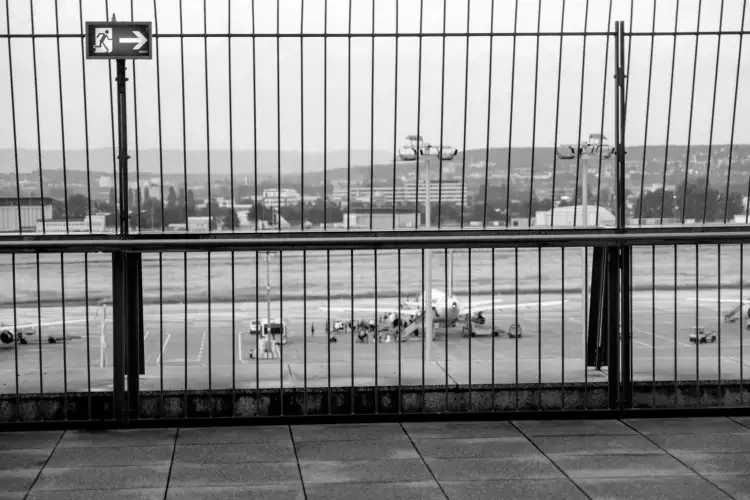 Schwarz-Weiß Aufnahme; zeigt einen Blick von der Besucher(:innen)-Plattform am Stuttgarter Flughafen mit dem durch ein Gitterzaun 